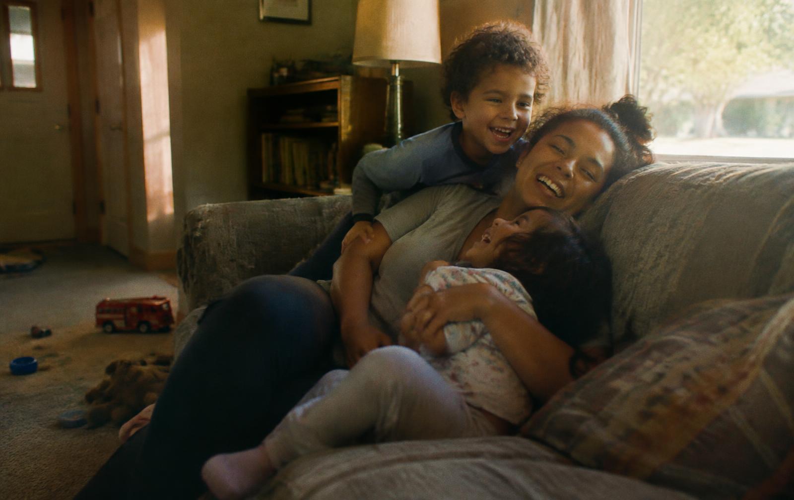 A mom laughing on the couch with her two kids